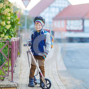 Little kid boy in helmet riding with his scooter in the city