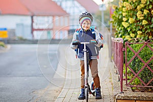 Little kid boy in helmet riding with his scooter in the city