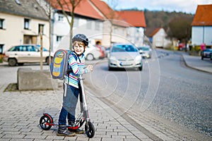 Little kid boy in helmet riding with his scooter in the city