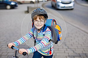 Little kid boy in helmet riding with his scooter in the city