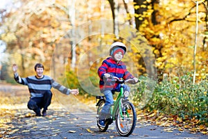 Little kid boy and his father in autumn park with a bicycle. Dad teaching his son biking