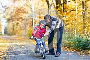 Little kid boy and his father in autumn park with a bicycle. Dad teaching his son biking