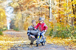 Little kid boy and his father in autumn park with a bicycle. Dad teaching his son biking