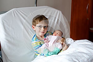 Little kid boy holding his sleeping newborn baby sister in hospital