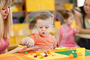 Little kid boy learning to use colorful play clay in kindergarten. Babies group studying in creche