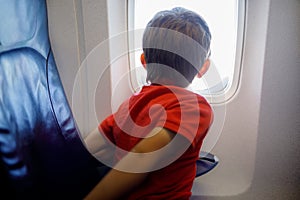 Little kid boy looking outside of plane window during flight on airplane.