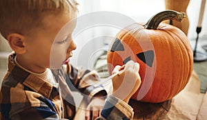 Little kid  boy making jack-o-lantern at home, drawing scary face on pumpkin