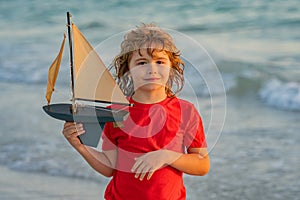 Little kid boy play with toy boat in the sea waves at the beach during summer vacation. Childhood and summer family