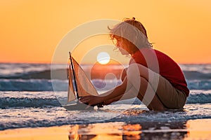 Little kid boy play with toy boat in the sea waves at the beach during summer vacation. Dream on travel. Sea dream