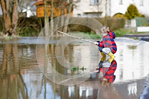 Little kid boy playing with fishing rod by puddle