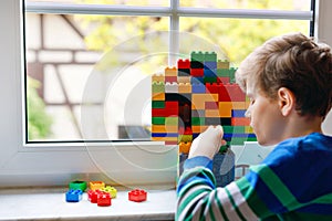 Little kid boy playing with lots of colorful plastic blocks. Adorable school child having fun with building and creating