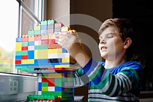 Little kid boy playing with lots of colorful plastic blocks. Adorable school child having fun with building and creating