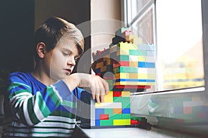 Little kid boy playing with lots of colorful plastic blocks. Adorable school child having fun with building and creating