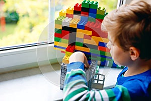 Little kid boy playing with lots of colorful plastic blocks. Adorable school child having fun with building and creating