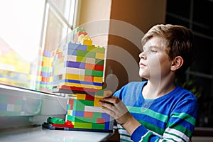 Little kid boy playing with lots of colorful plastic blocks. Adorable school child having fun with building and creating