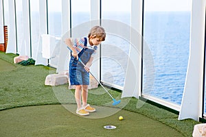 Little kid boy playing mini golf on a cruise liner.