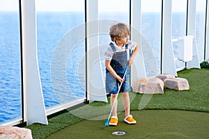 Little kid boy playing mini golf on a cruise liner.