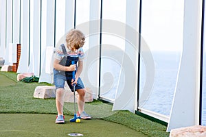 Little kid boy playing mini golf on a cruise liner.