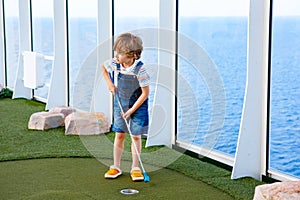 Little kid boy playing mini golf on a cruise liner.