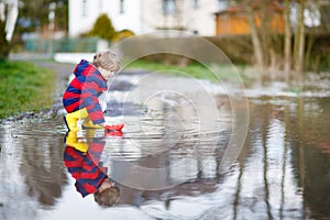 Little kid boy playing with paper boat by puddle