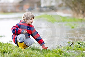 Little kid boy playing with paper boat by puddle