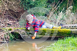 Little kid boy playing with paper boat by puddle