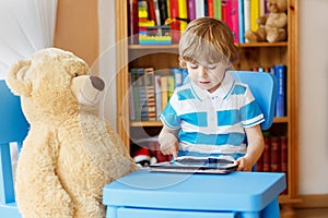 Little kid boy playing with tablet computer in his room at home