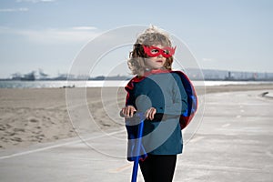Little kid boy plays superhero. Child on scooter in park. Kids learn to skate roller board. Little boy skating.