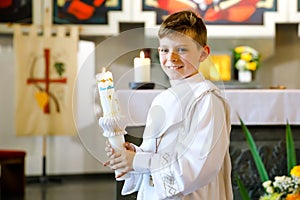 Little kid boy receiving his first holy communion. Happy child holding Christening candle. Tradition in catholic curch