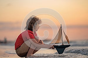 Little kid boy sailing toy ship on sea water. Summer vacation with kids. Kid dreaming about sailing. Concept of