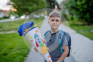 Little kid boy with school satchel on first day of school, holding school cone with gifts