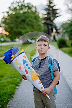 Little kid boy with school satchel on first day of school, holding school cone with gifts