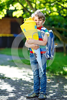 Little kid boy with school satchel on first day to school, holding school cone with gifts