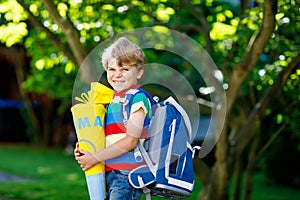 Little kid boy with school satchel on first day to school, holding school cone with gifts