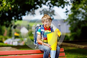 Little kid boy with school satchel on first day to school, holding school cone with gifts