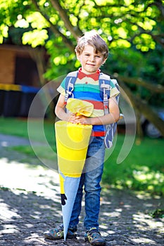 Little kid boy with school satchel on first day to school, holding school cone with gifts