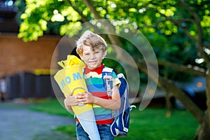Little kid boy with school satchel on first day to school, holding school cone with gifts