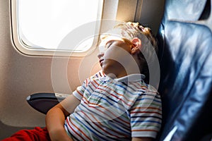 Little kid boy sleeping during long flight on airplane. Child sitting inside aircraft by a window