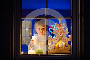 Little kid boy standing by window at Christmas time and holding