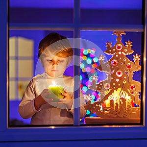 Little kid boy standing by window at Christmas time and holding