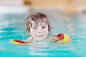 Little kid boy with swimmies learning to swim in an indoor pool