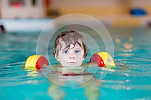 Little kid boy with swimmies learning to swim in an indoor pool