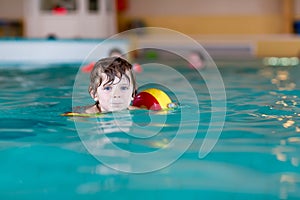 Little kid boy with swimmies learning to swim in an indoor pool