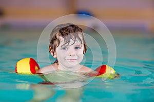 Little kid boy with swimmies learning to swim in an indoor pool