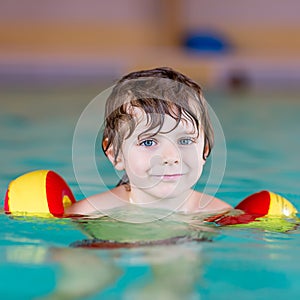 Little kid boy with swimmies learning to swim in an indoor pool