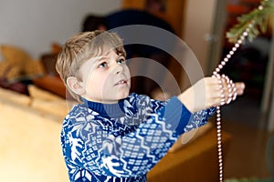 Little kid boy taking down holiday decorations from Christmas tree. Father on background