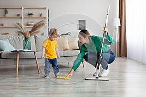 Little kid boy watching her mother mopping the floor after him. Woman wiping the floor with rag next to her baby