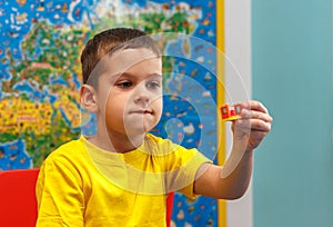 Little kid boy in yellow t-shirt playing with lots of colorful plastic blocks indoor. Child having fun with building and creating