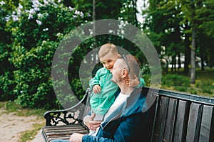 Little kid boy and young father sitting together in colorful clothing on bench in park. Happy family of two