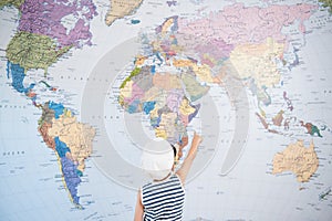 Little kid in captain cap pointing at world map with finger direction tour